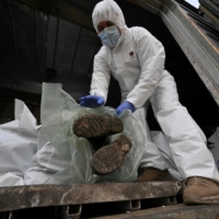 Ukrainian forensics experts examine the body of a Russian soldier exhumed in the village of Zavalivka, west of Kyiv, in a refrigerated rail car stacked with the Russian war dead on Wednesday. | AFP-JIJI