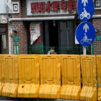 A resident looks out from behind barriers at a fruit shop in Shanghai on Monday.  | REUTERS 