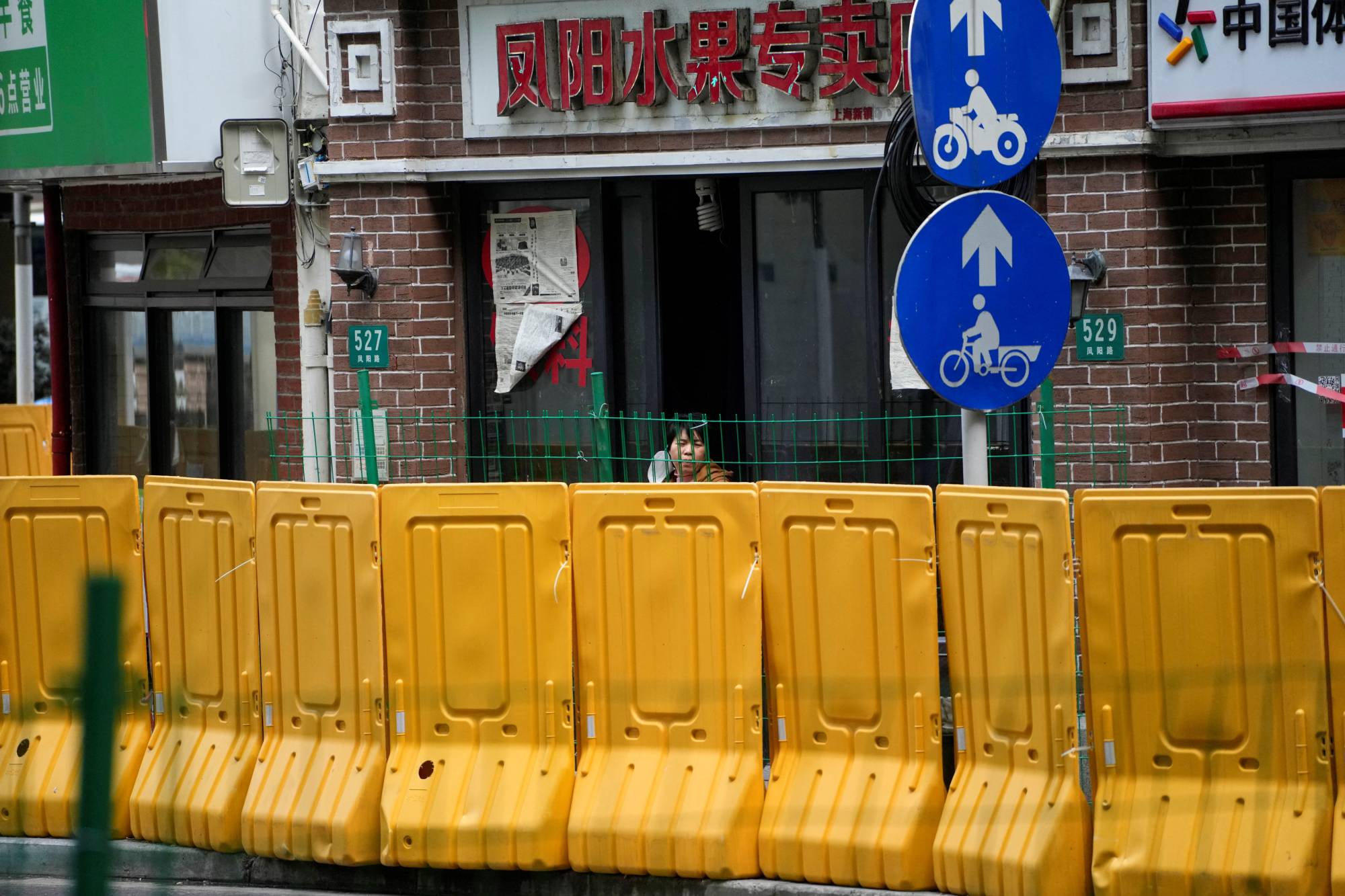 A resident looks out from behind barriers at a fruit shop in Shanghai on Monday.  | Reuters 