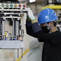 A worker moves a stack of lithium-ion batteries for an electric minivehicle on the production line at Mitsubishi Motors\' Mizushima plant in Kurashiki, Okayama Prefecture, on Thursday. | BLOOMBERG