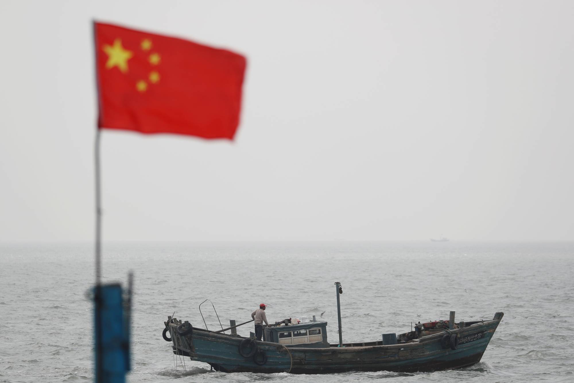 A Chinese flag is seen near a fishing boat off the coast of Qingdao, China. Members of the 'Quad' alliance plan to use satellite technology to create a tracking system for illegal fishing from the Indian Ocean to the South Pacific by connecting surveillance centers in Singapore and India. | REUTERS
