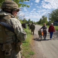 Local women walk along a street while Ukrainian servicemen patrol an area in the town of Kurakhove, in the Donetsk region, Ukraine, on May 20. | REUTERS