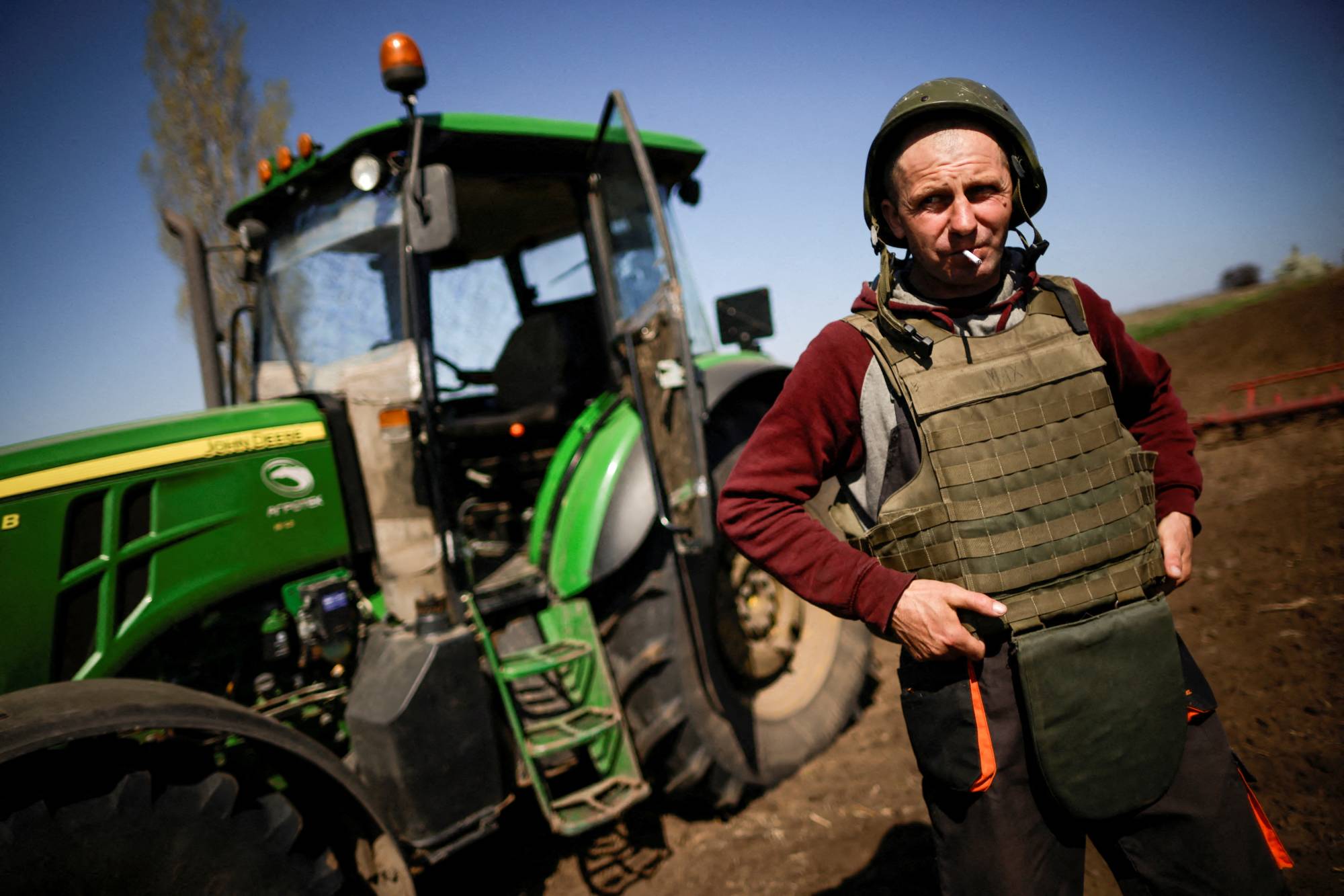 A Ukrainian farmer, wearing body armor and a helmet, works at the topsoil in a field in the Zaporizhzhia region of Ukraine on April 26. | REUTERS
