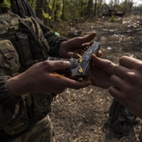 Ukrainian soldiers examine a handgun salvaged from the backpack of a Russian soldier found in an abandoned tank in the Seversky Donets River near Sievierodonetsk, Ukraine, on Wednesday. | IVOR PRICKETT / THE NEW YORK TIMES