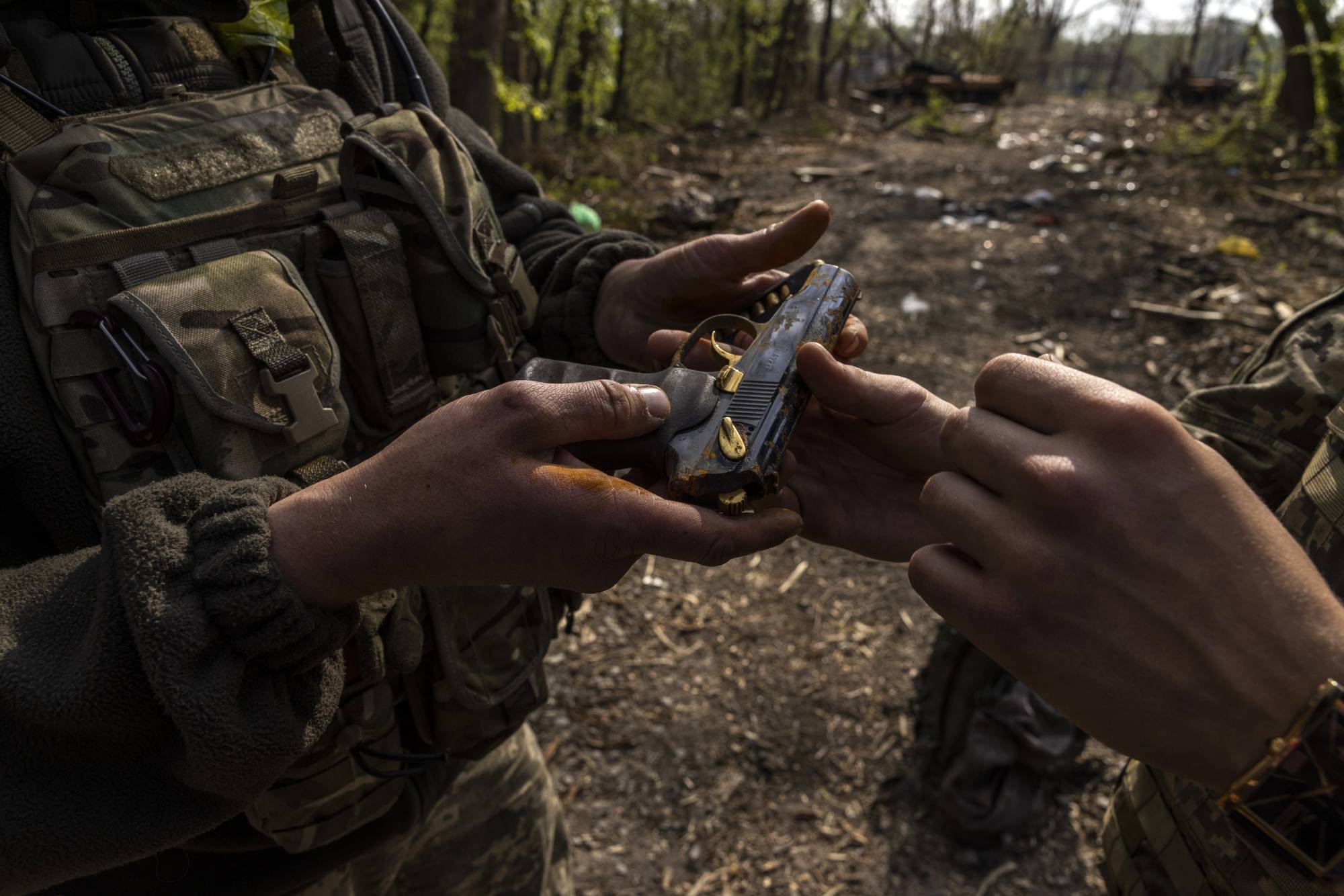 Ukrainian soldiers examine a handgun salvaged from the backpack of a Russian soldier found in an abandoned tank in the Seversky Donets River near Sievierodonetsk, Ukraine, on Wednesday. | Ivor Prickett / The New York Times
