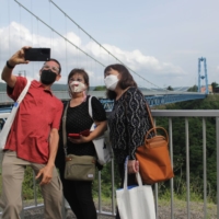 Tourists from Hawaii take a selfie at Ryujin Suspension Bridge in Ibaraki Prefecture on Thursday during a test tour. | BLOOMBERG