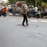 A man struggles to cross a road after his slippers got stuck in melted tar on a hot day in Ahmedabad, India.  | REUTERS