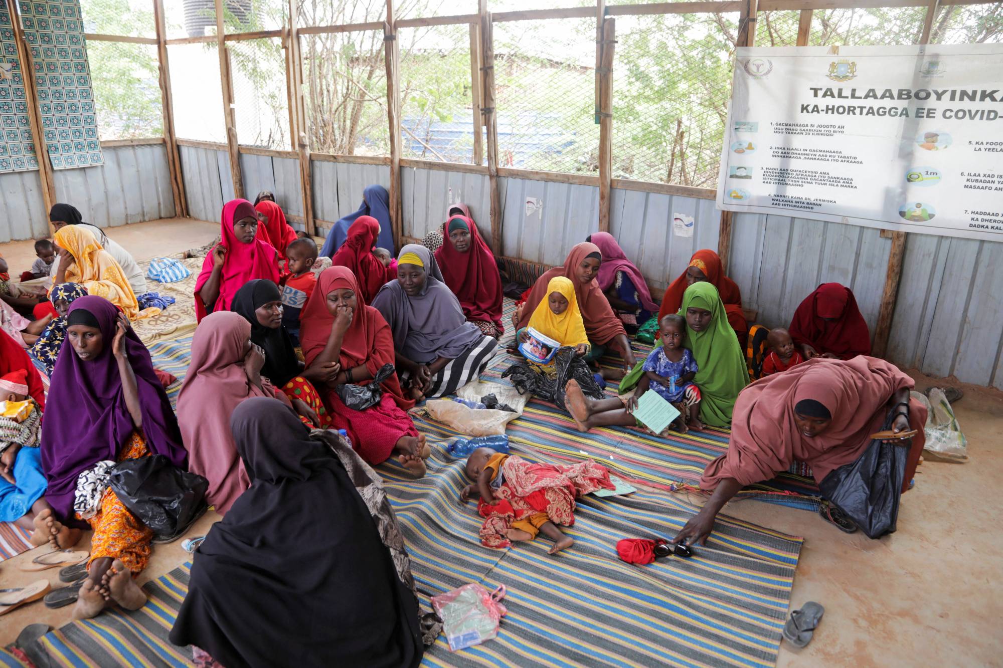 Internally displaced Somali women sit with their children as they wait for malnutrition screening in Dollow, Gedo Region, Somalia, on May 24. Humanitarian agencies already struggling with widespread price increases under the pandemic say the crisis in Europe has made things worse. | REUTERS