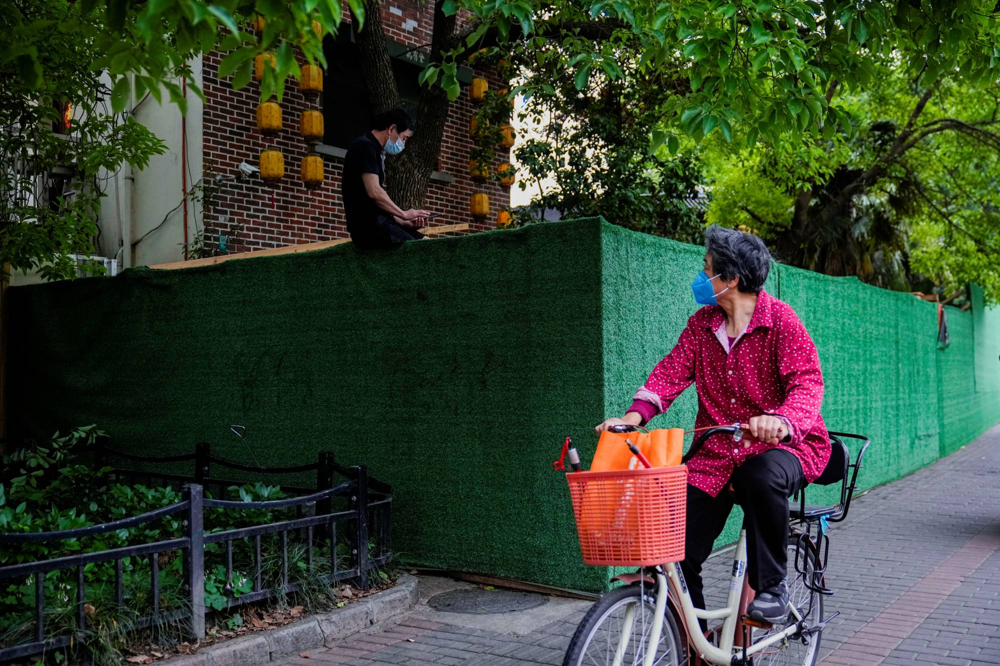 A cyclist notices a resident sitting on a barrier at a closed residential area during a COVID-19 lockdown in Shanghai on Monday. | REUTERS