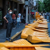 People stand next to barriers in the Jing\'an district of Shanghai on Tuesday, as the city prepared to lift COVID-19 curbs after two months of heavy-handed virus restrictions. | AFP-JIJI