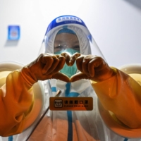 A health worker makes a heart with her hands while waiting to take swab samples from people in the Jing\'an district of Shanghai on Tuesday as the city prepared to lift more curbs after two months of heavy-handed restrictions.  | AFP-JIJI