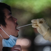 A health worker takes a swab sample from a man in the Jing\'an district of Shanghai on Tuesday as the city prepared to lift a COVID-19 lockdown after two months of heavy-handed restrictions.  | AFP-JIJI