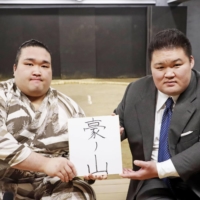Newly promoted jūryō wrestler Nishikawa (left) presents his new ring name, Gonoyama, alongside Takekuma stablemaster (ex-ozeki Goeido) at Takekuma stable in Tokyo\'s Ota ward on May 25. | JAPAN SUMO ASSOCIATION