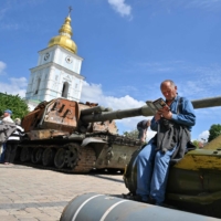 An elderly man reads a book at an open air exposition of destroyed Russian equipment in the center of Kyiv on Wednesday. | AFP-JIJI