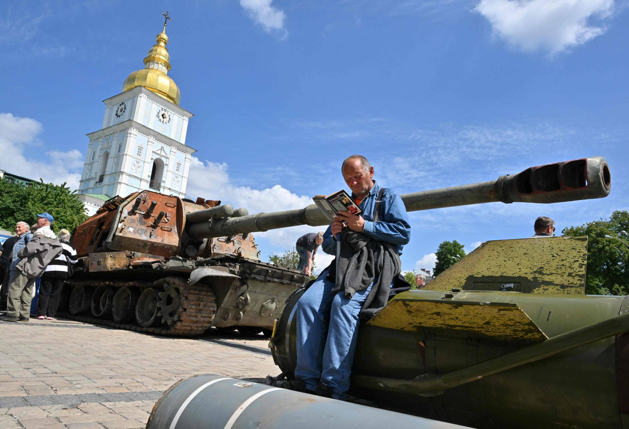 An elderly man reads a book at an open air exposition of destroyed Russian equipment in the center of Kyiv on Wednesday. | AFP-JIJI