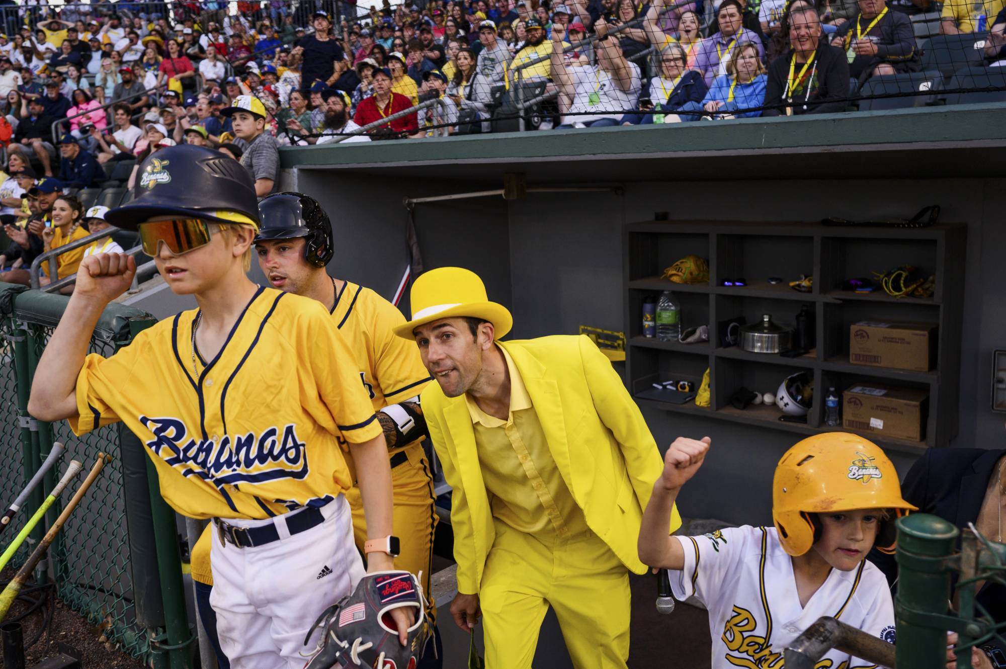 Jesse Cole, center in yellow tux, the owner of the Savannah Bananas, in the dugout for a road game with the Kansas City Monarchs, in Kansas City, May 7, 2022. TikTok choreography, dancing umpires, a ballet-trained first-base coach: This collegiate summer league team has amassed a big following by leaning into entertainment. | Shawn Brackbill / The New York Times 