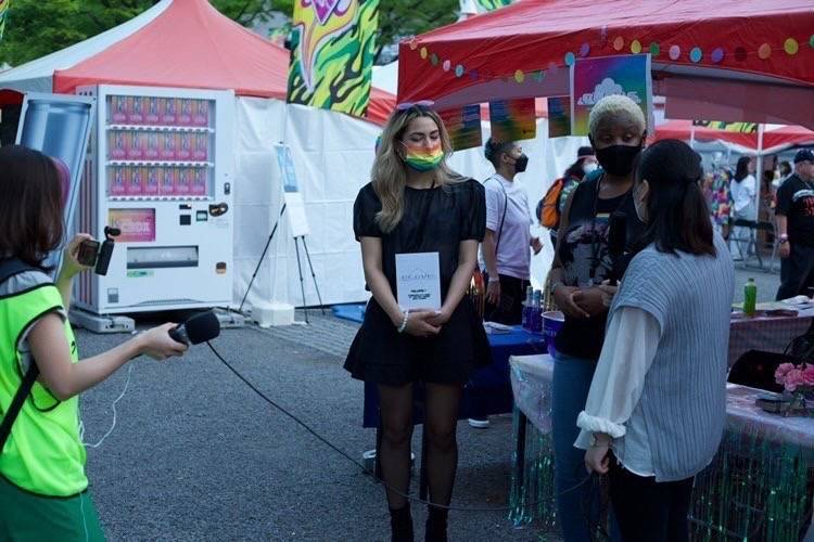 Reyna Marquez (left) and Chloe Douglas (center) are interviewed for Japanese TV at their Tokyo Rainbow Pride booth in April.  | LAM YIK FEI / THE NEW YORK TIMES