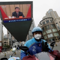 A delivery worker rides near a giant screen showing Chinese President Xi Jinping at an event celebrating the 100th anniversary of the founding of the Chinese Communist Youth League in Beijing, in May. | REUTERS