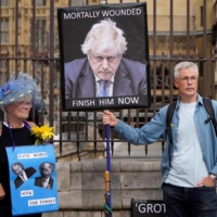 Demonstrators hold placards picturing British Prime Minister Boris Johnson in front of Parliament in London on Monday. | AFP-JIJI