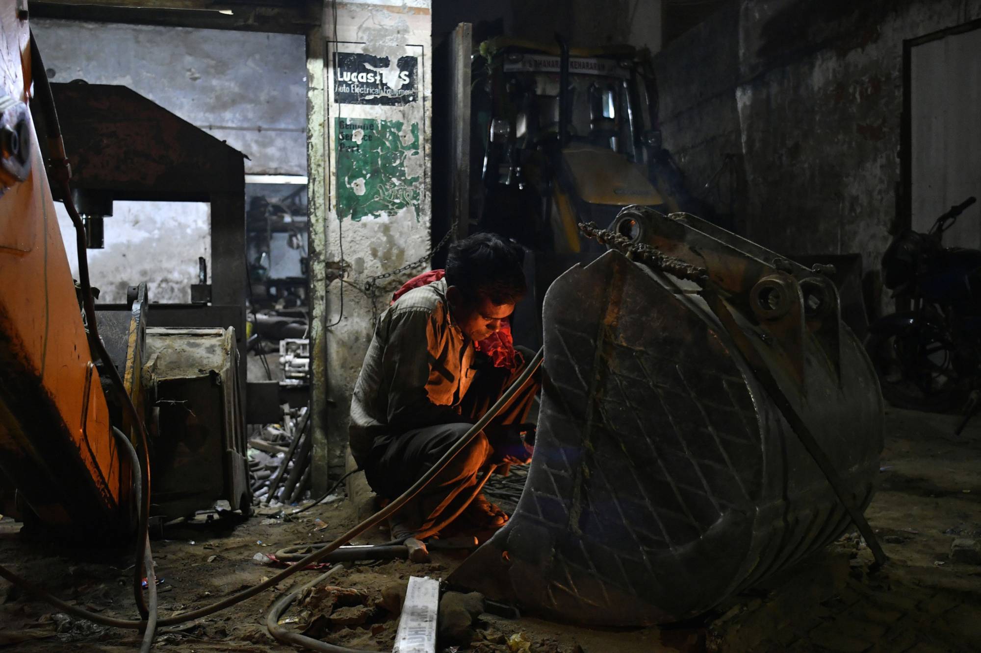 A worker welds an excavator bucket at a heavy machinery repair workshop in Ahmedabad, Gujarat, India, in November 2017. | Bloomberg