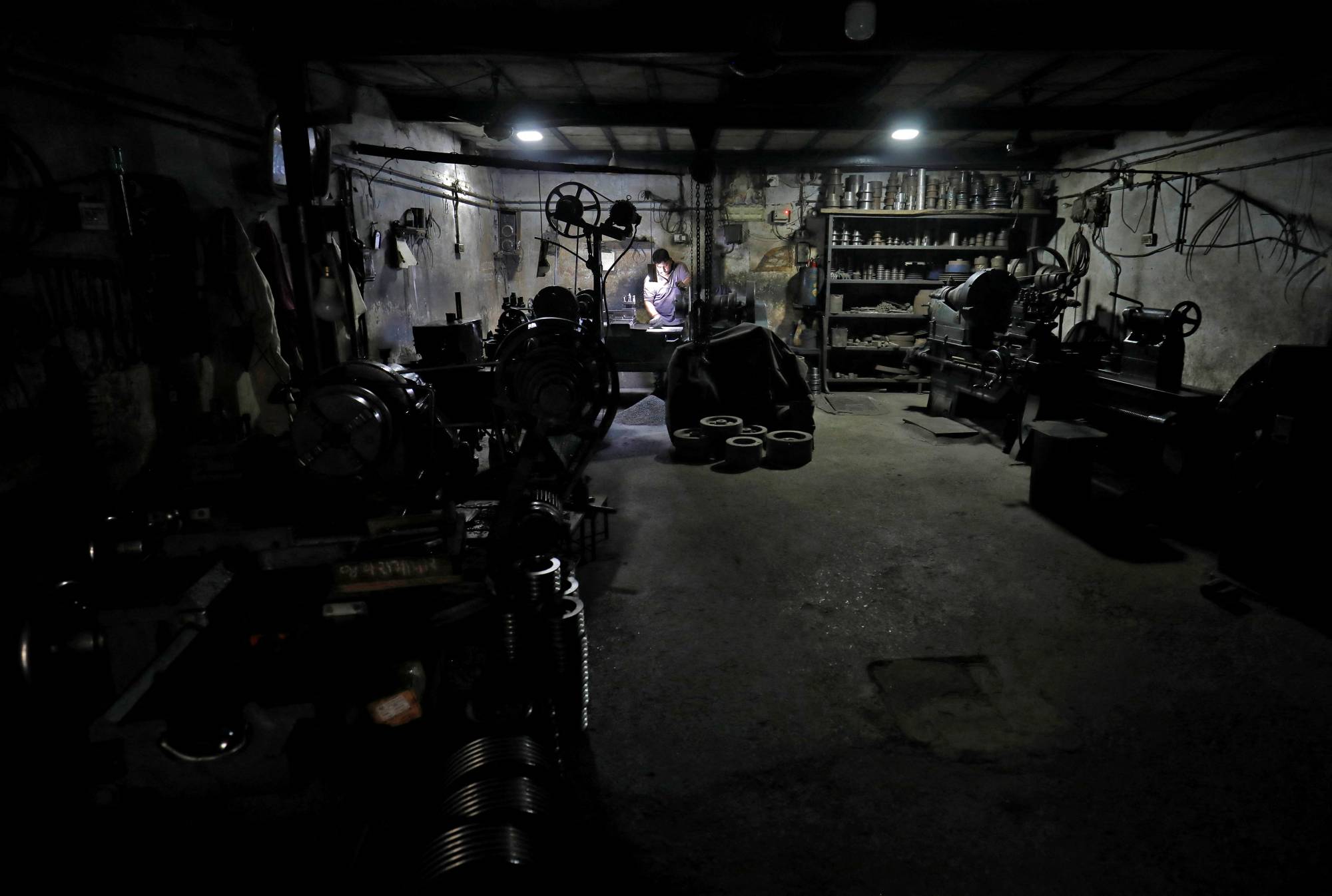 A worker operates a lathe machine as he fixes a gear box at a small scale manufacturing unit in Ahmedabad, India, on May 28. | REUTERS