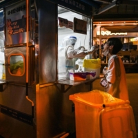 A health worker in a cabin takes a swab sample from a man on a street in the Jing\'an district of Shanghai on Sunday. | AFP-JIJI