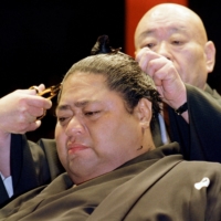 Hawaiian-born former ozeki Konishiki fights back tears as his stablemaster Takasago cuts off his topknot in a retirement ceremony at Ryogoku Kokugikan on May 30, 1998. | REUTERS