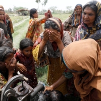 Women and children wash themselves after work at a muskmelon farm at a hand pump on the outskirts of Jacobabad, Pakistan, on May 17. | REUTERS