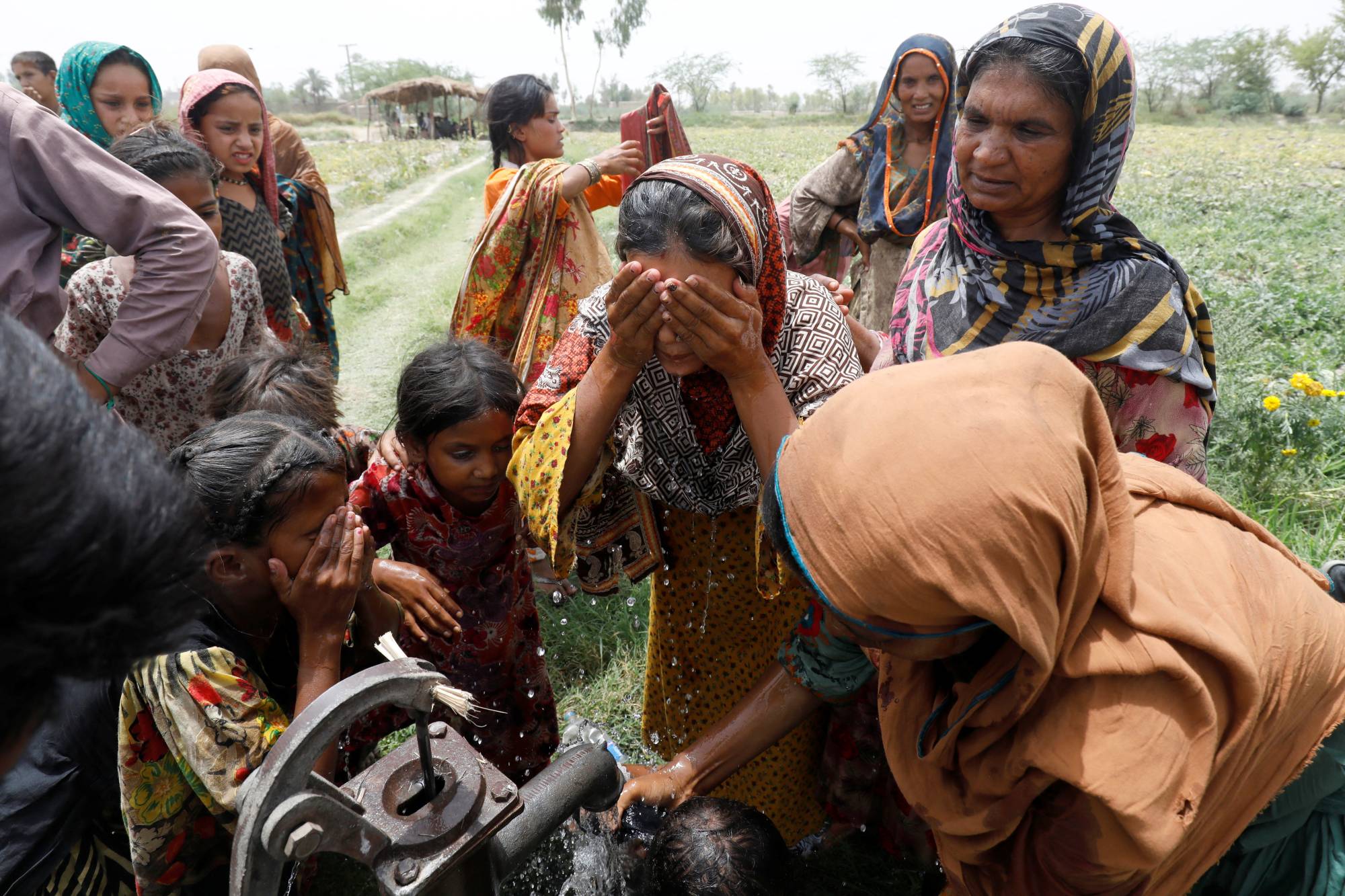 Women and children wash themselves after work at a muskmelon farm at a hand pump on the outskirts of Jacobabad, Pakistan, on May 17. | REUTERS