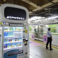 A trial to reproduce platform announcements and the sounds of train arrivals and departures onto a screen is held above a vending machine at Ueno Station on Wednesday. | KYODO