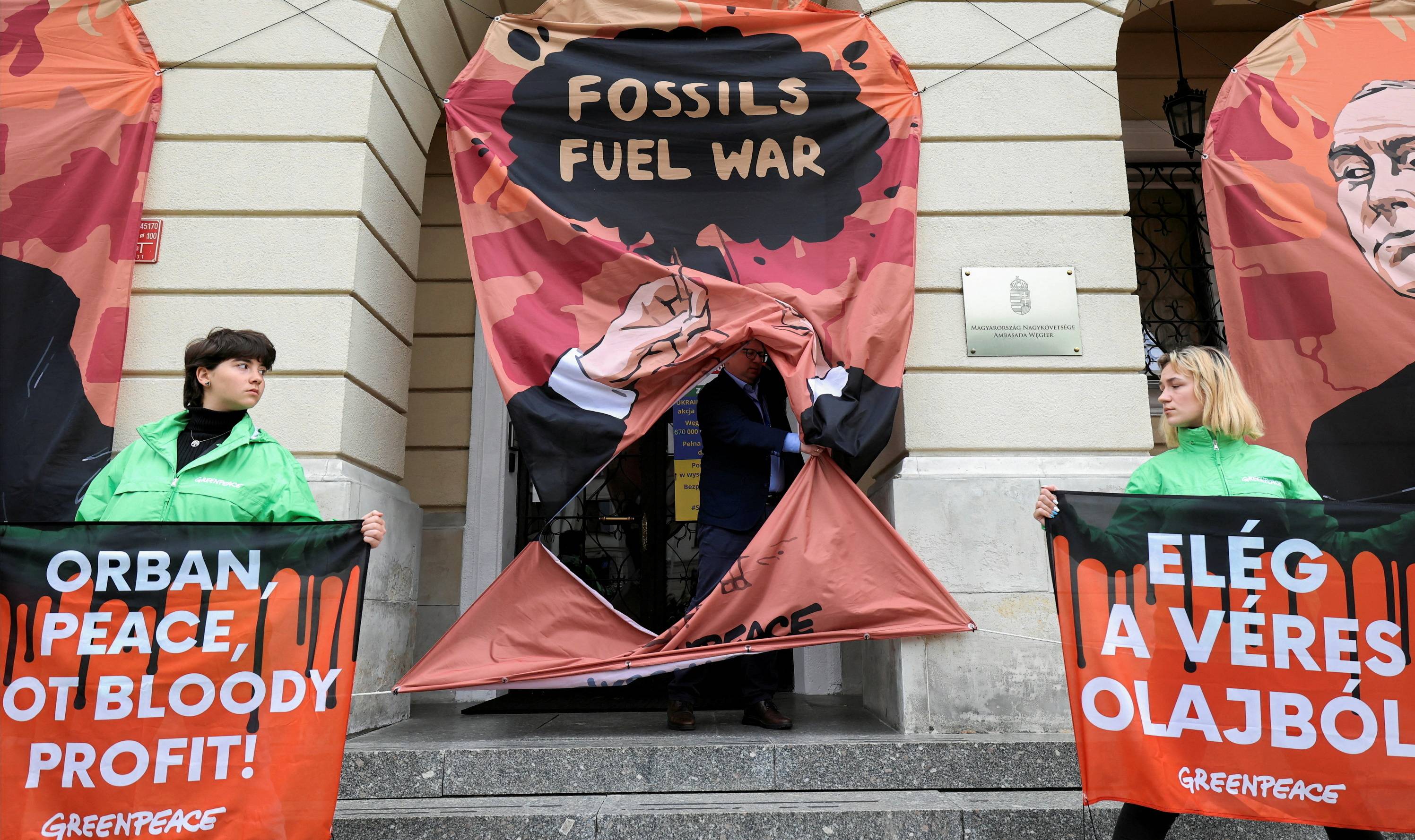 Greenpeace activists hold banners with slogans in English and Hungarian during a protest against Hungarian fossil fuel supplies from Russia, in front of the Hungarian embassy in Warsaw on May 25. The slogan in Hungarian reads: 'Enough of the red oil.' | REUTERS 