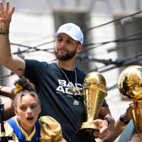 Warriors guard Stephen Curry (center) holds his Finals MVP trophy as he waves from a bus during the team\'s championship parade in San Francisco on Monday. | AFP-JIJI