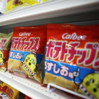 Calbee potato chips are displayed at the company\'s headquarters in Tokyo in June 2013. The company has already raised prices several times this year due to a bad potato crop and higher material costs. To the dismay of chip lovers, it also had to cut down bag sizes. | BLOOMBERG