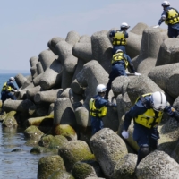 Police officers search coastal areas in Shibetsu, Hokkaido, on May 16, with Kunashiri Island seen in the background, for clues on people who went missing after a tourist boat sank off Hokkaido in April. | KYODO
