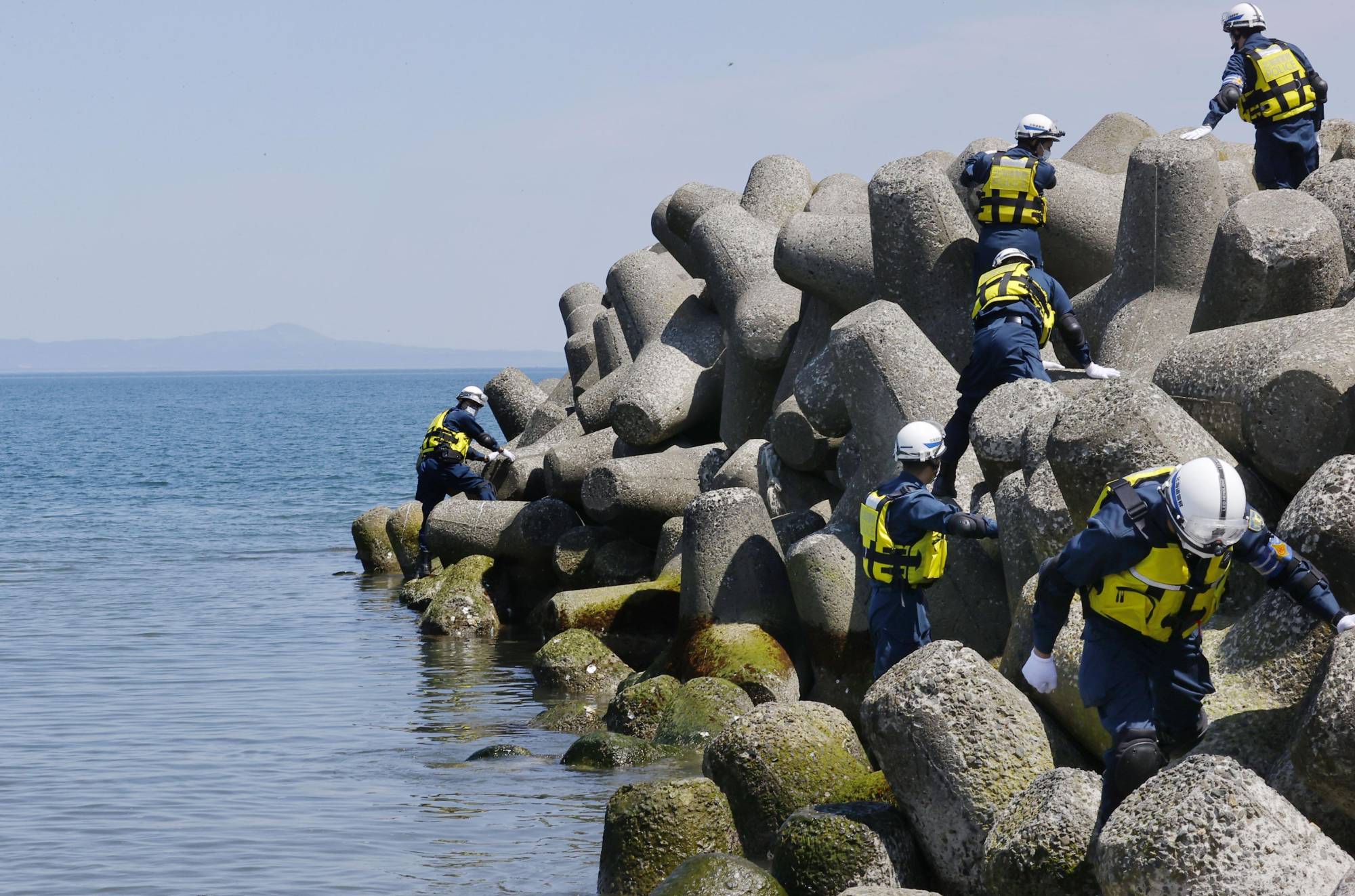 Police officers search coastal areas in Shibetsu, Hokkaido, on May 16, with Kunashiri Island seen in the background, for clues on people who went missing after a tourist boat sank off Hokkaido in April. | KYODO