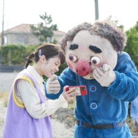 A middle-aged event worker (Tsuyoshi Muro) helps a young YouTuber (Yukino Kishii, left) with her video content until she rejects his request for money in Keisuke Yoshida’s “Kami wa Mikaeri o Motomeru.” | © 2022 ‘KAMI WA MIKAERI O MOTOMERU’ FILM PARTNERS
