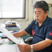 Shigenori Takenishi, head of the Yonaguni fisheries cooperative association, reviews the Fisheries Agency’s safety alert information on dangerous areas for fishing. | NISHINIPPON SHIMBUN