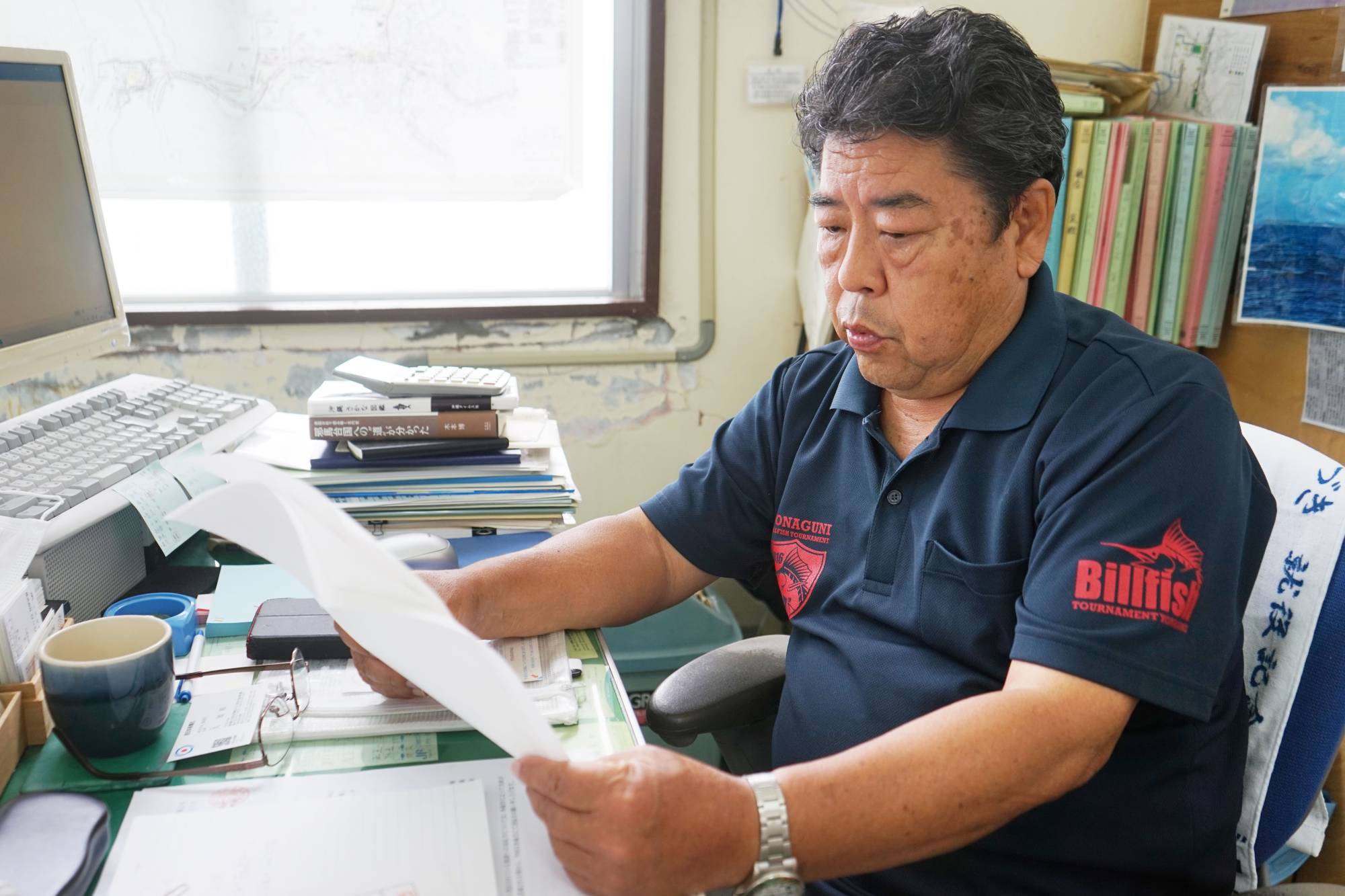 Shigenori Takenishi, head of the Yonaguni fisheries cooperative association, reviews the Fisheries Agency’s safety alert information on dangerous areas for fishing. | Nishinippon Shimbun