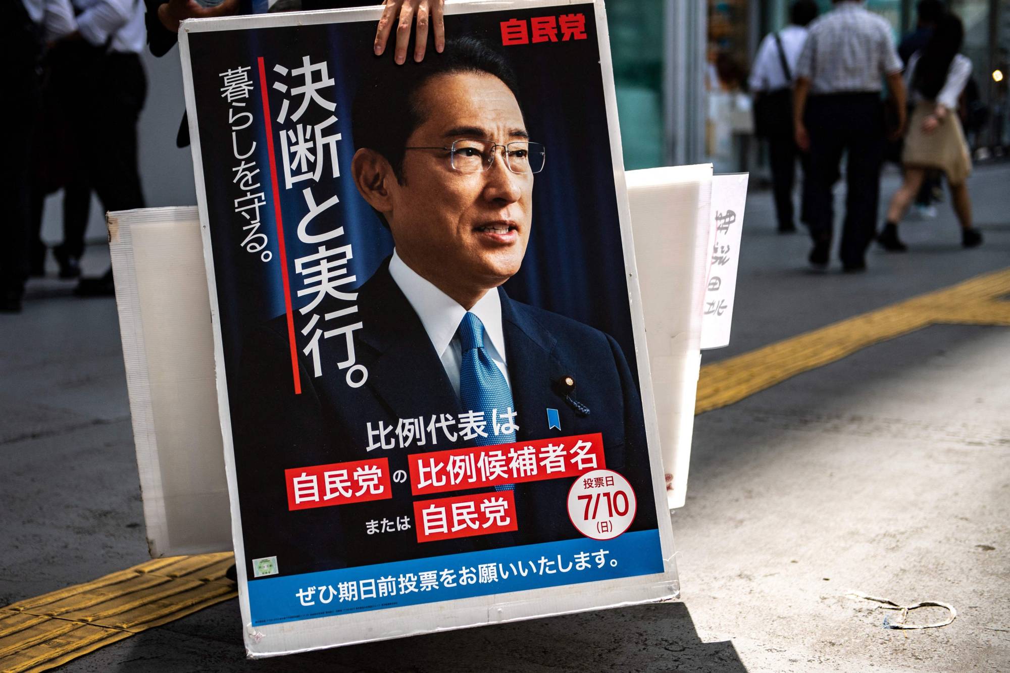 A voter holds a placard showing Kishida after a campaign stop by Liberal Democratic Party member Keiichiro Asao in Yokohama on June 24. | AFP-JIJI