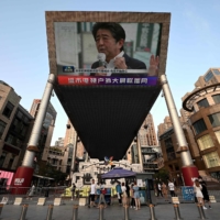 A large video screen shows news broadcast featuring an image of  Abe in Beijing on Friday. | AFP-JIJI