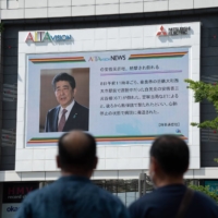 Passersby in Shinjuku, Tokyo, view news of the shooting of Shinzo Abe on Friday. | BLOOMBERG
