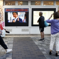 Pedestrians in Tokyo watch a news broadcast about the assassination of Abe on Friday. | BLOOMBERG