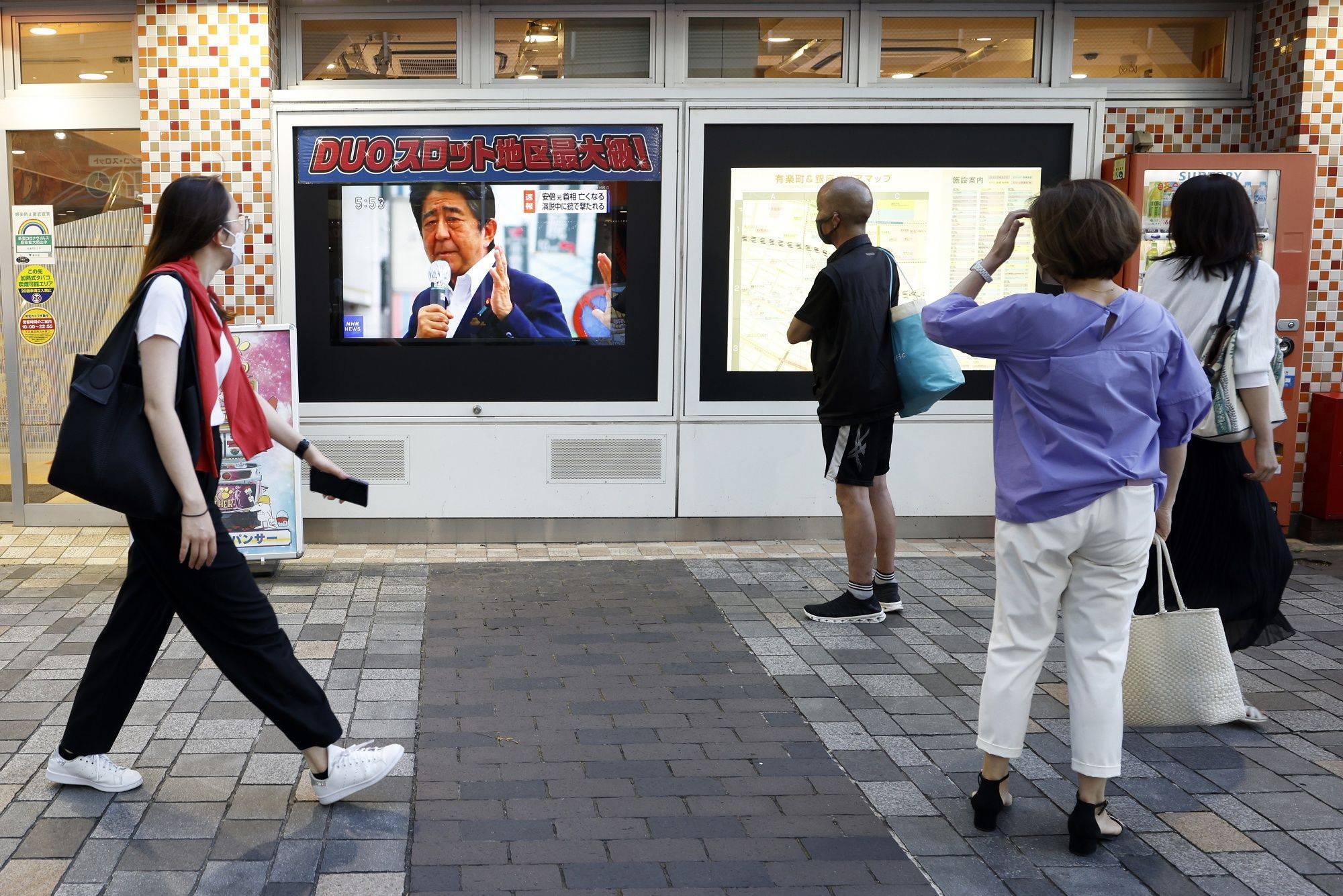 Pedestrians in Tokyo watch a news broadcast about the assassination of Abe on Friday. | BLOOMBERG