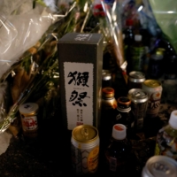 Dassai, a sake made in late former Prime Minister Shinzo Abe\'s home base of Yamaguchi Prefecture is seen Saturday among tributes laid at the site where he was shot a day earlier near Yamato-Saidaiji Station in the city of Nara while campaigning for a parliamentary election. | REUTERS
