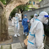 Workers in Shanghai wear protective suits last month amid the COVID-19 outbreak. | REUTERS