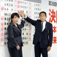 Prime Minister Fumio Kishida and Liberal Democratic Party policy chief Sanae Takaichi place a flower next to a victorious candidate\'s name  at the party\'s headquarters in Tokyo on Sunday. | KYODO