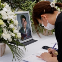 A mourner signs a book in front of a portrait of late former Prime Minister Shinzo Abe on an altar at the Liberal Democratic Party headquarters in Tokyo on Monday. | REUTERS
