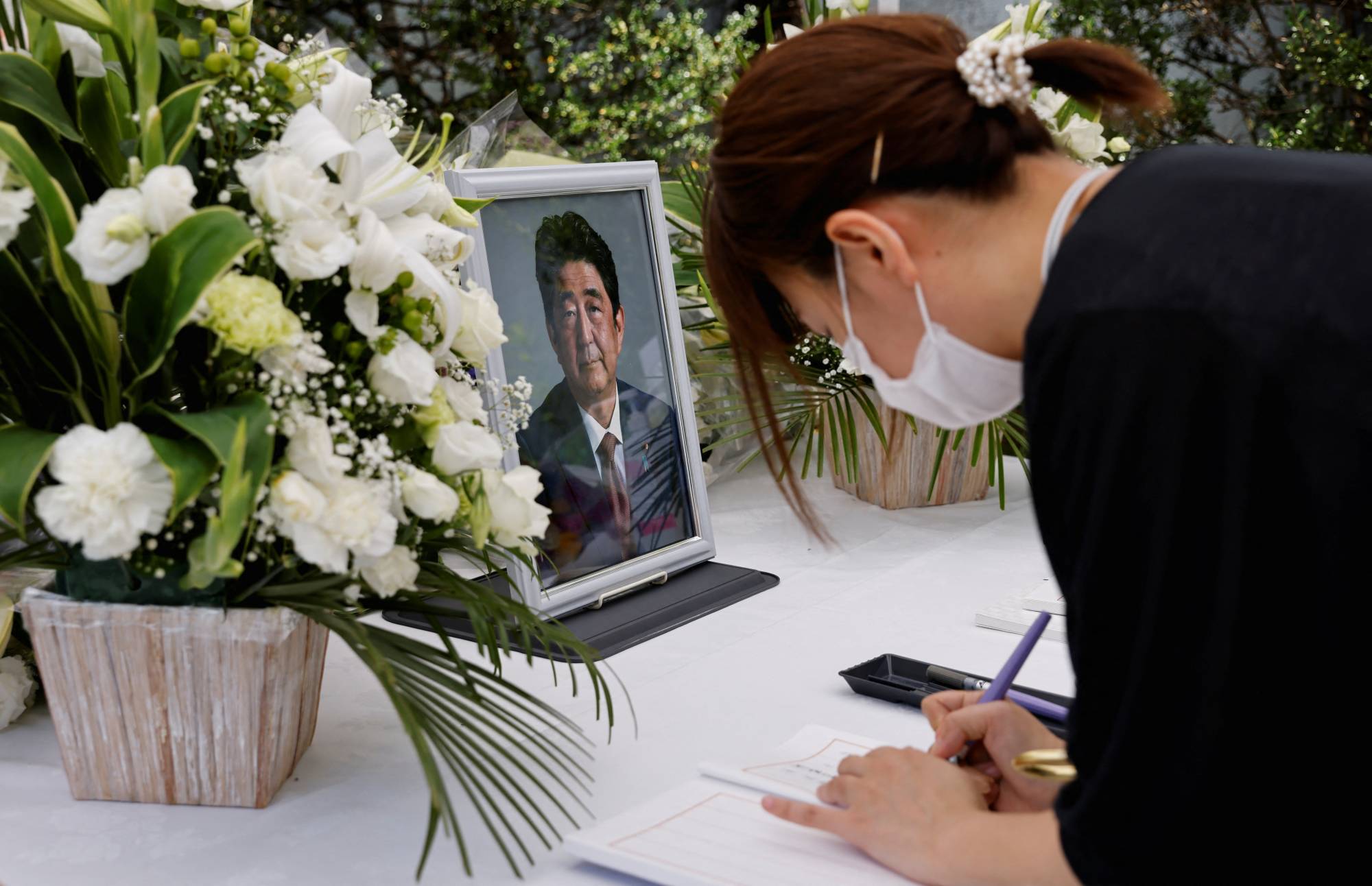 A mourner signs a book in front of a portrait of late former Prime Minister Shinzo Abe on an altar at the Liberal Democratic Party headquarters in Tokyo on Monday. | REUTERS