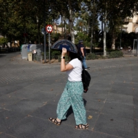 A woman uses a fan to cover her head from the sun and heat as she takes a walk in Seville, Spain, on Wednesday. | REUTERS