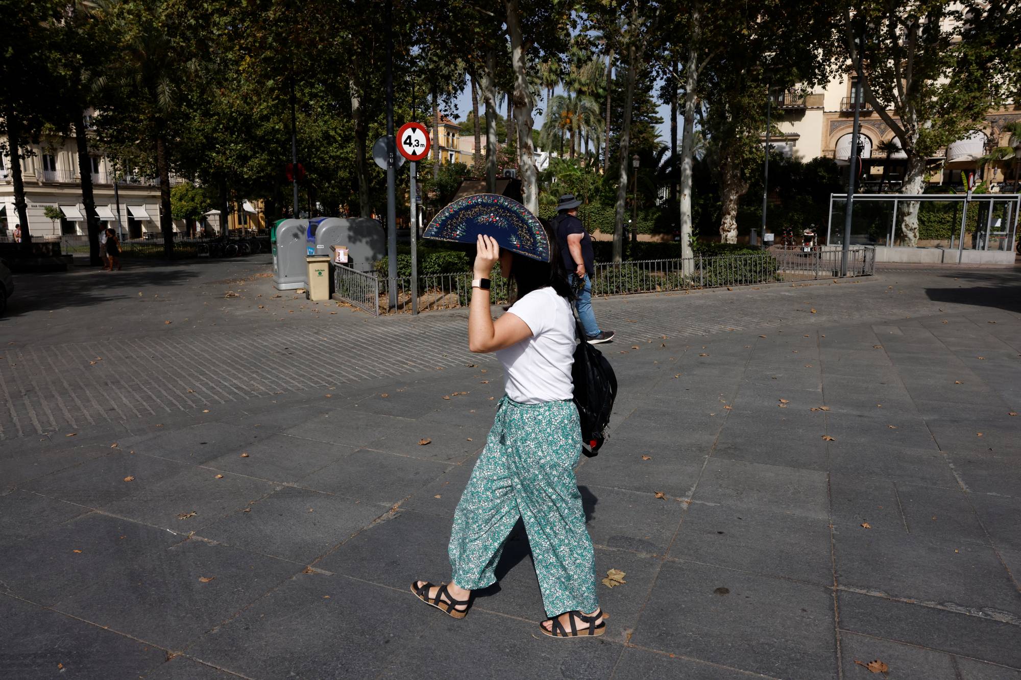 A woman uses a fan to cover her head from the sun and heat as she takes a walk in Seville, Spain, on Wednesday. | REUTERS
